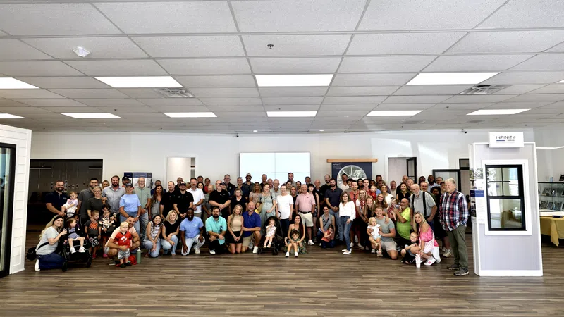 Large diverse group of people posing together in a spacious room with wood flooring and bright ceiling lights