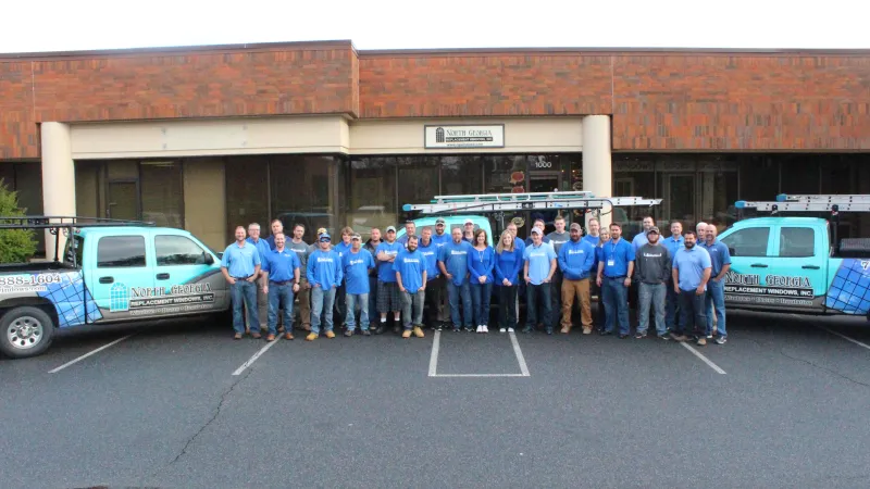 Group of workers in blue shirts standing between two company trucks outside a brick office building.