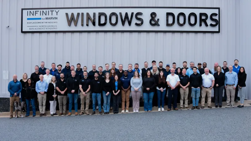 Group photo of Infinity Windows & Doors employees standing in front of company building and sign.