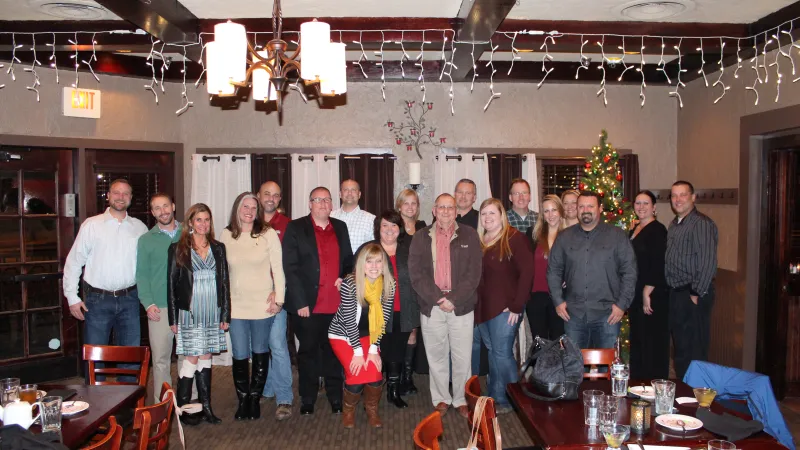Group of people posing inside a decorated room with Christmas tree and string lights hanging from ceiling