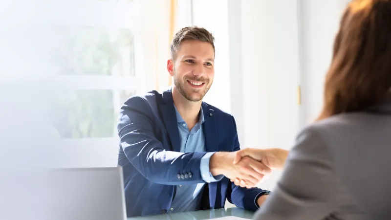 Two professionals shaking hands in a bright office setting, symbolizing business agreement and partnership.