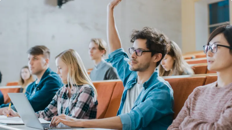 College students sitting in lecture hall with one student raising his hand to ask a question.