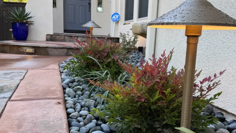 Modern front yard with stone landscaping, outdoor lamp, and a gray entry door under a covered porch.