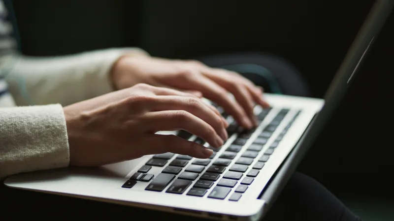Close-up of hands typing on a laptop keyboard with a blurred dark background.