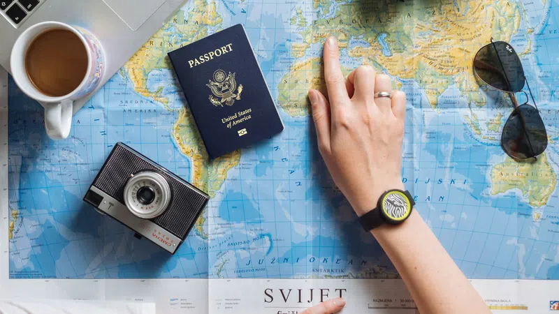 Person planning travel with world map, passport, laptop, cameras, sunglasses, and coffee on white table