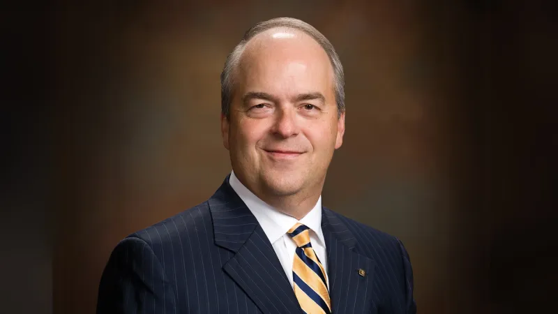Portrait of a professional man in a pinstripe suit, smiling confidently against a blurred background.