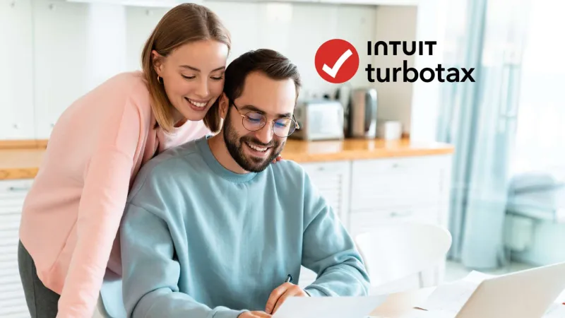 Couple reviewing documents and smiling at home with laptop, representing Intuit TurboTax tax preparation.