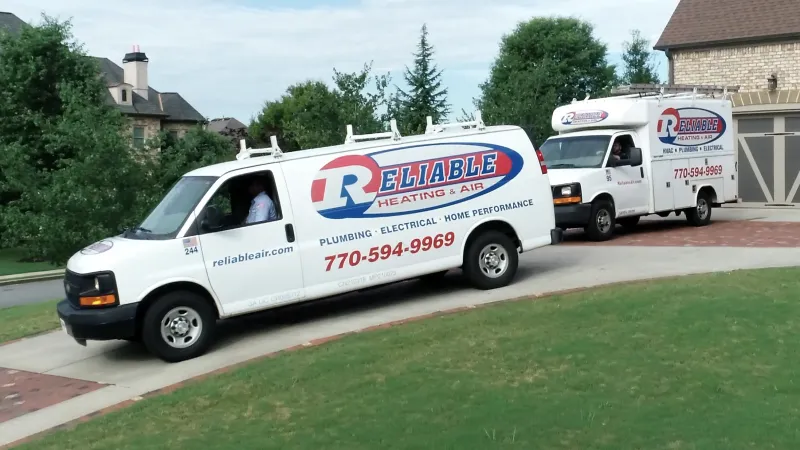 Two Reliable Heating and Air service vans parked in a residential area, showcasing company branding and services.