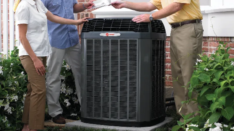 A technician discusses an air conditioning unit installation with a couple outside their home surrounded by greenery.