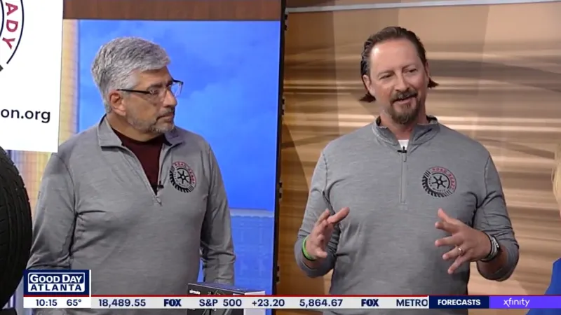 Two men in gray quarter-zip sweatshirts with logos speaking on a Good Day Atlanta TV segment.
