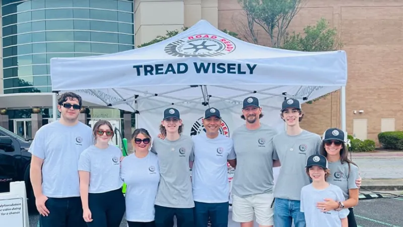 Group of nine people wearing matching Tread Wisely shirts and hats standing under a Tread Wisely tent outdoors.
