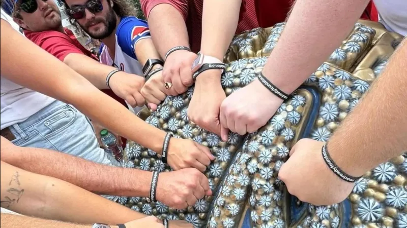 Group of people wearing matching black wristbands with messages, showing unity with hands together.