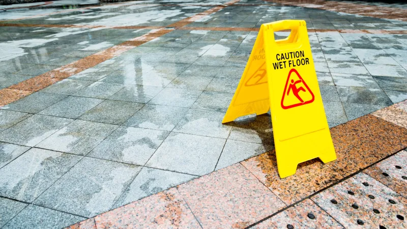 Yellow caution wet floor sign on wet tiled outdoor surface indicating slippery conditions