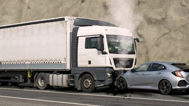 Collision between a silver car and a white truck with cracked windshield and smoke on a road.