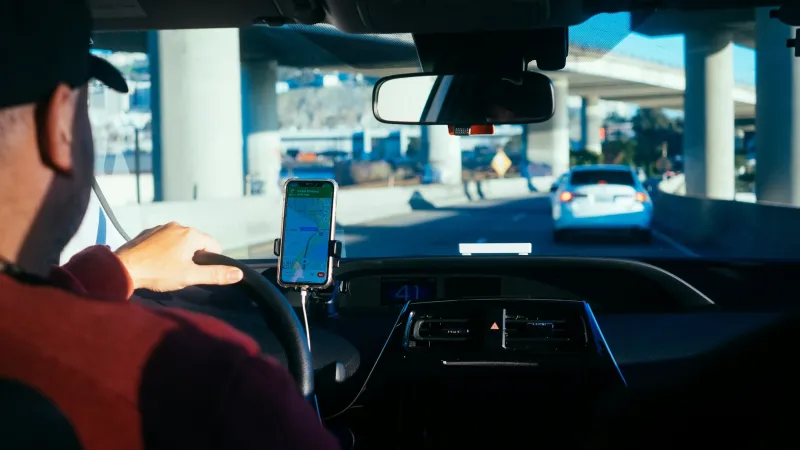 Driver using smartphone GPS navigation while driving on a city highway underpass during daytime.