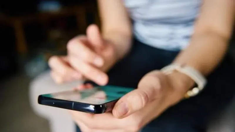 Person using smartphone with one hand holding the phone and the other tapping the screen.