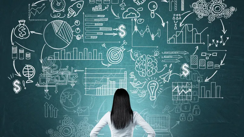 Businesswoman standing with hands on hips looking at chalkboard with hand-drawn charts and graphs
