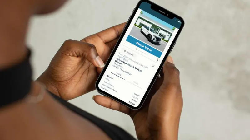 Person holding smartphone showing Volkswagen Atlas 2.0T Peak Edition car listing with price and video option.