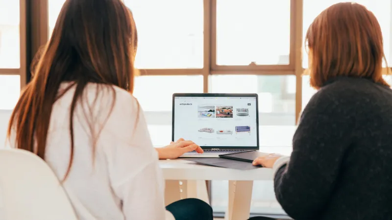 women sitting at a table looking at a laptop