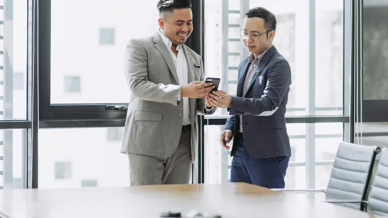 a couple of men in suits looking at a cell phone