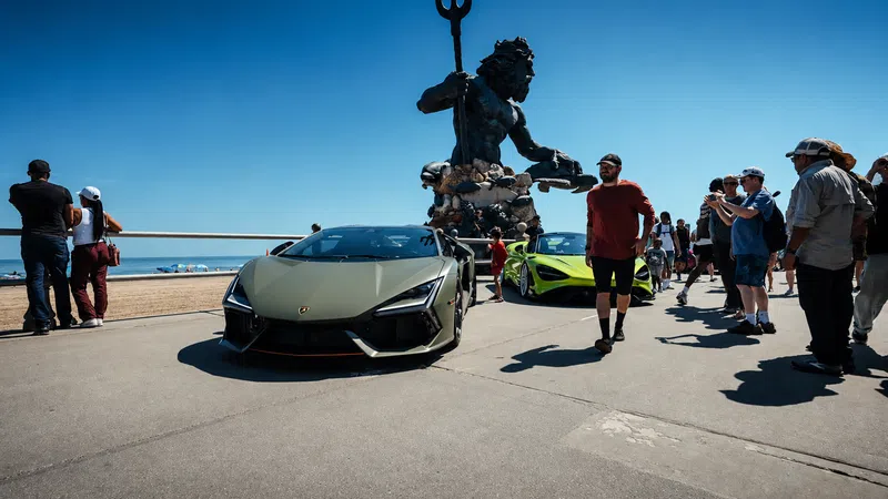 Matte green Lamborghini and lime green sports car parked by a beach with a large Poseidon statue and people gathered.