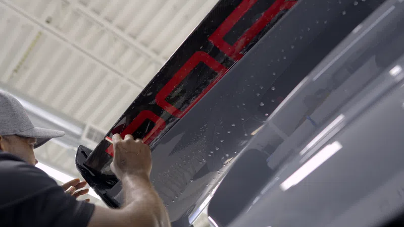 Person applying black and red decal to the wing of an aircraft inside a hangar with bright lighting.