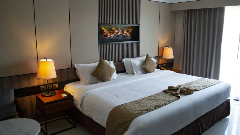 Modern hotel room with king-size bed, bedside lamps, decorative pillows, wall art, and floor-to-ceiling curtains.