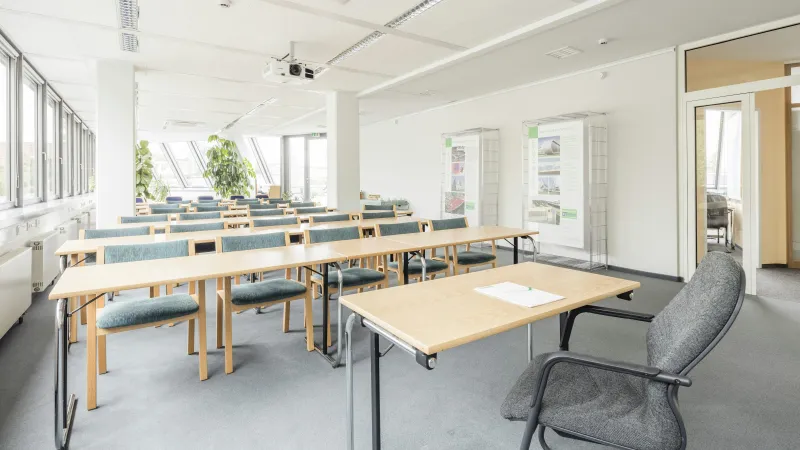 Bright modern classroom with rows of wooden desks and green chairs under white ceiling with projector.