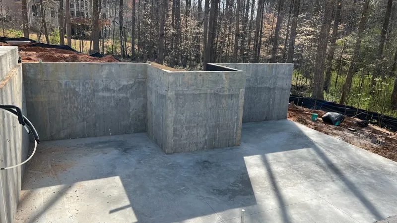 Concrete foundation walls and slab for a new house under construction in a wooded residential area.