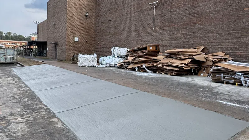 Freshly poured concrete pavement next to brick building with cardboard and white wrapped waste piles.