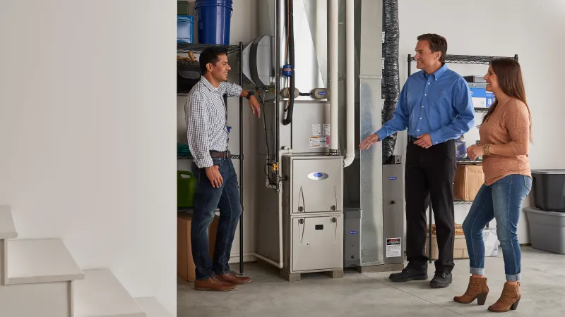 HVAC technician explaining furnace system to a couple in a modern home basement with organized storage