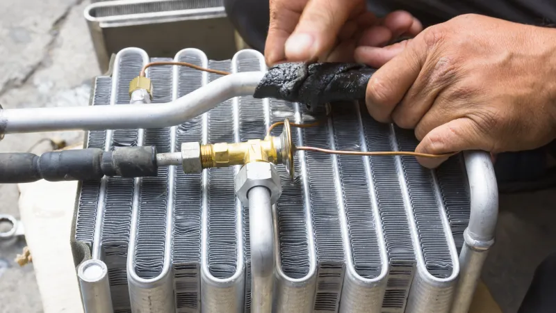 Hand repairing aluminum air conditioner condenser coil with black insulating tape and copper piping close-up
