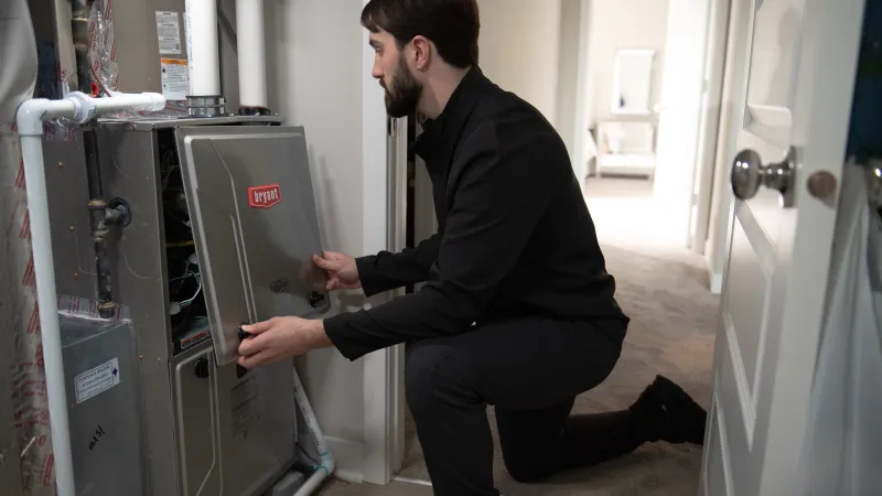 Technician in black uniform inspecting and opening a Bryant heating system panel in a residential home.