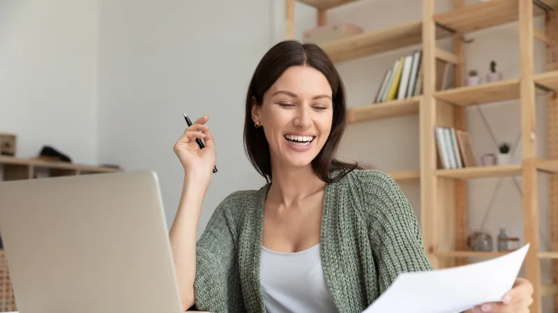 Happy young woman working from home with laptop and documents in cozy office space