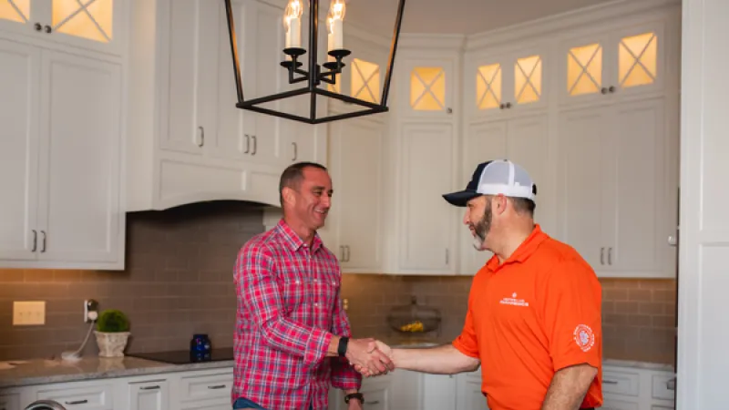 Two men shaking hands in a modern kitchen with white cabinets and granite countertops.