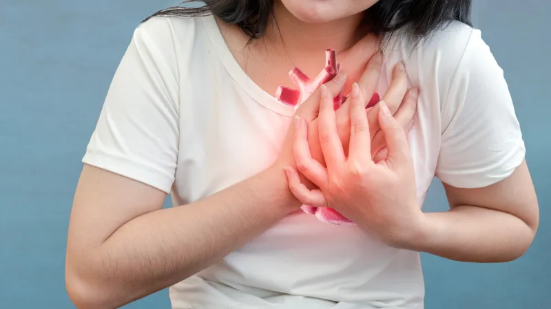A person clutching their chest, symbolizing heart pain or discomfort, with a glowing heart graphic.