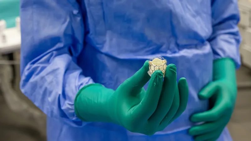 A medical professional in scrubs holds a small, round cell culture in gloved hands.