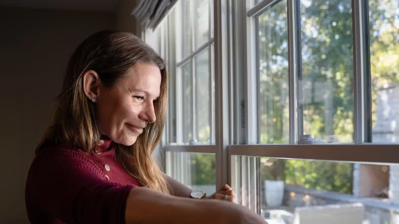 Woman measuring window dimensions using a tape measure with natural outdoor light through glass panes.