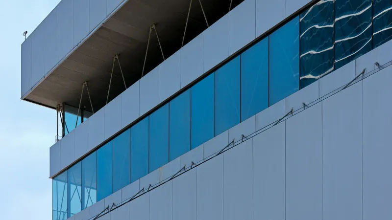 Modern building facade with large blue-tinted windows and white panels under a clear sky.