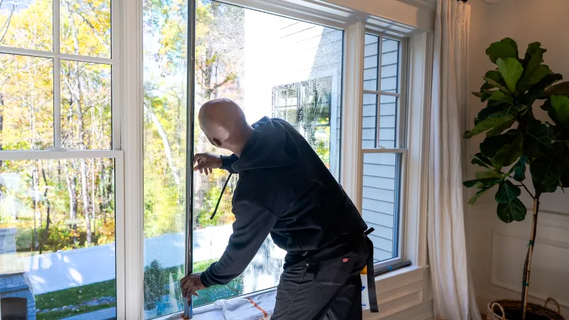Person cleaning a large window inside a bright room with a squeegee on a sunny day.
