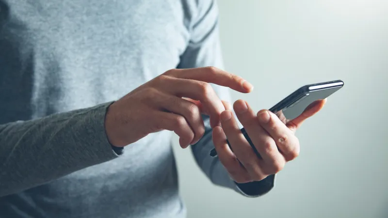Person in gray long sleeve shirt using a smartphone with focused hand gestures on a light background