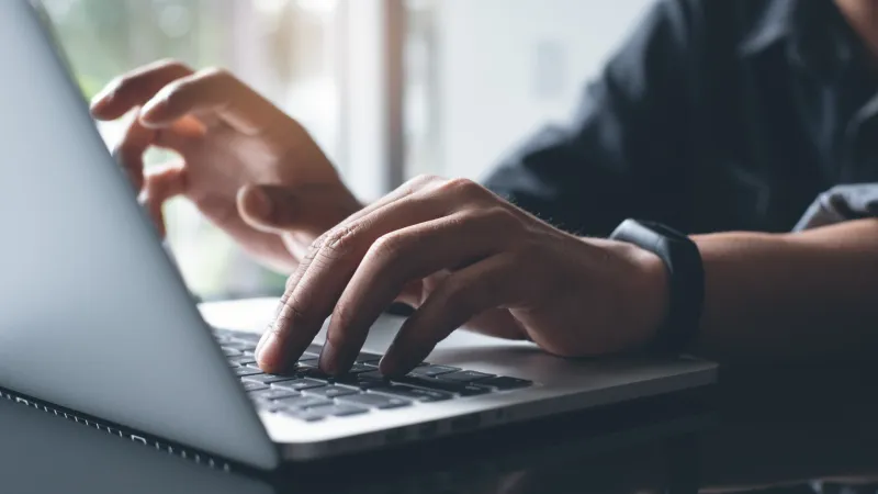 Close-up of hands typing on a laptop keyboard with a wristwatch, reflecting on a glossy surface.