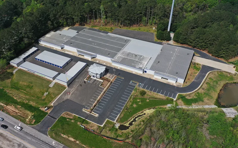 Aerial view of a large warehouse complex surrounded by trees and a clear blue sky.