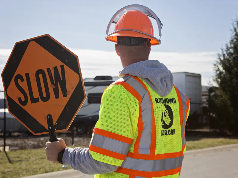 Man in high-visibility gear holding a slow sign to manage traffic safety