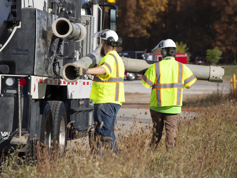 Two men carrying equipment to perform sub-surface utility engineering