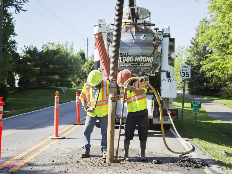 Two men from Blood Hound Underground Utility Locators providing vacuum excavation services on the road