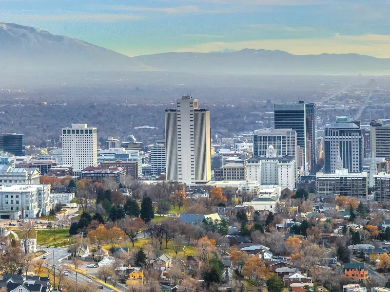 City skyline with high-rise buildings, residential areas, and mountains in the background under a cloudy sky