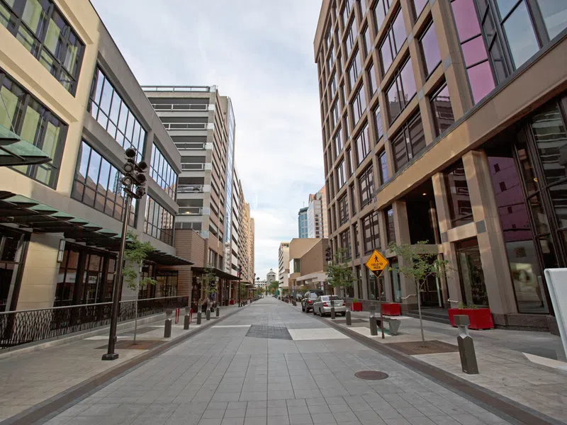 Wide pedestrian-friendly urban street lined with modern office buildings under a cloudy sky.