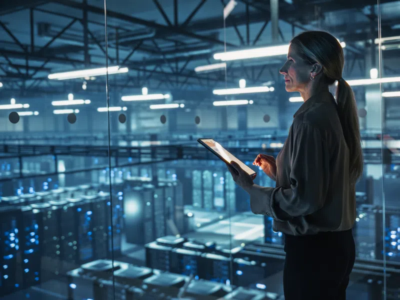 Woman using digital tablet in a modern data center with servers and blue lighting at night