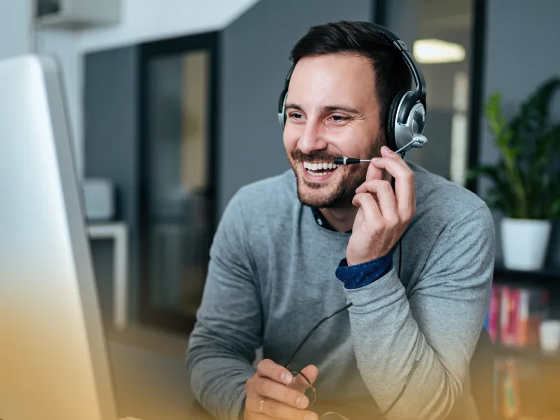 Smiling man wearing headset working on computer in modern office setting with plants and shelves in background